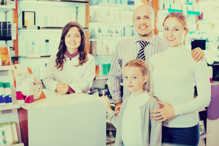 Cheerful smiling family of three happy persons getting help of a pharmacist in the pharmacyの写真素材