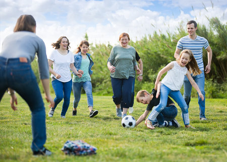 Cheerful males and females kicking the ball on green lawnの写真素材