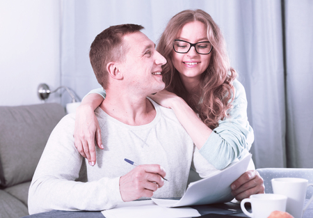 Smiling middle-aged husband and wife signing agreement papers together at homeの写真素材