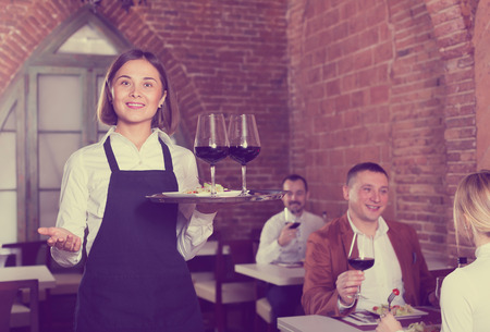 Nice female waiter showing country restaurant to visitorsの写真素材