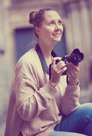 Young girl holding the camera in hands and photographing at a cityの写真素材