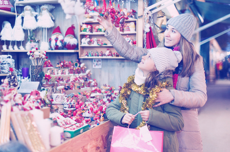 Young girl and her mother are choosing Christmas decorations in the market outdoor.の写真素材
