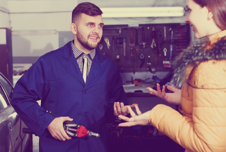 Young woman is asking master about repair her car in workshop.の写真素材