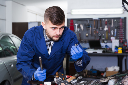  positive master is standing near table and looking on tools for repair in workshop.の写真素材