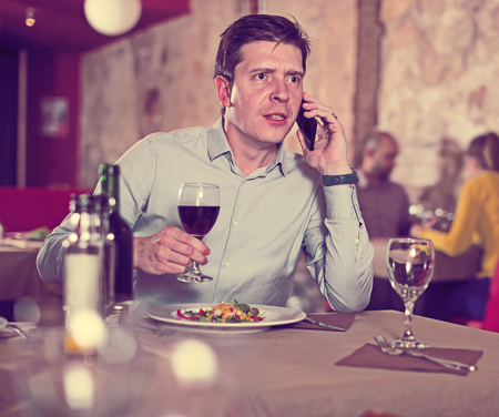 Glad man talking on phone during evening meal at restaurantの写真素材