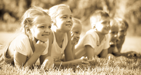 Group of positive kids in elementary school age lying on green grass in parkの写真素材