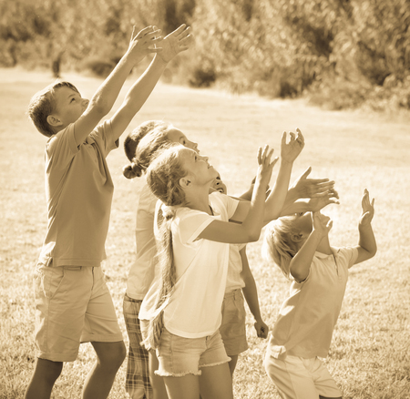 Group of laughing cheerful children having fun and jumping together on green grass in parkの写真素材