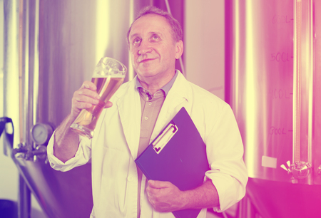 Man expert with folder is analizying the quality of beer in flask in laboratory.の写真素材