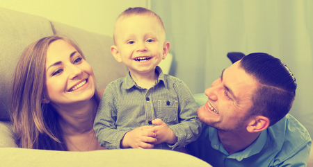 Portrait of cheerful happy young family sitting on sofa at homeの写真素材