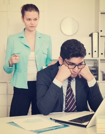 Young stressed businessman in office with dissatisfied female colleague behindの写真素材