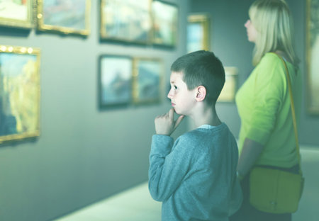 positive european mother and son looking at paintings in halls of museum