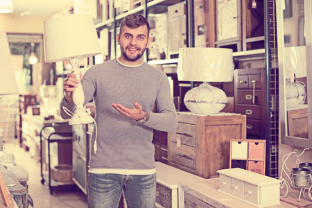 Young man satisfied with purchase of stylish table lamp in furniture storeの写真素材