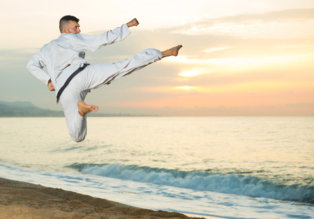 Positive sportive guy doing karate poses at  sunset sea shoreの写真素材