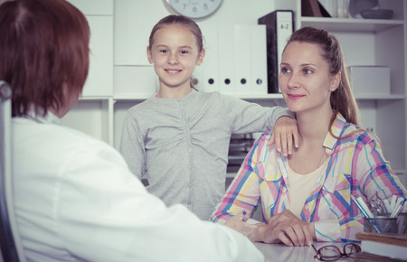 Portrait of mature medical worker talking with mother and daughterの写真素材