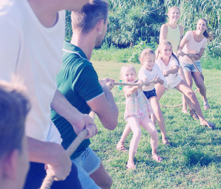 two families playing active games in summer park, tugging war