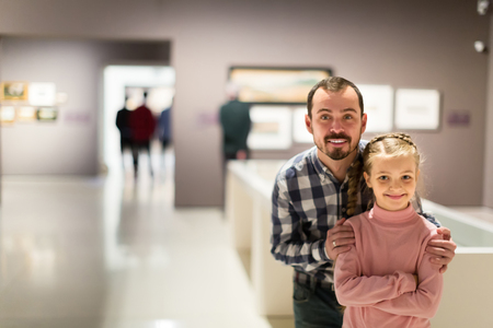 Positive man and small daughter looking paintings in museumの写真素材