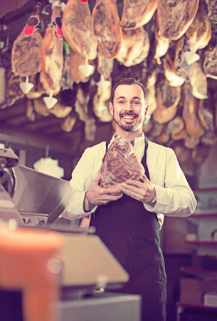 smiling european male shop assistant demonstrating piece of meat in butcherâs shopの写真素材