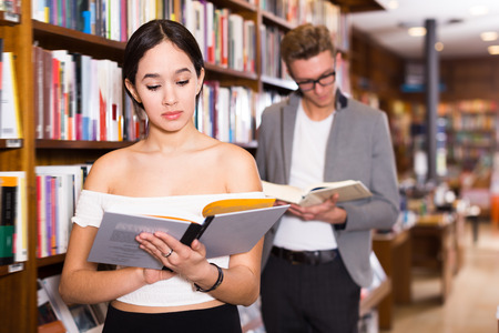 Happy girl reading interesting book in bookshopの写真素材