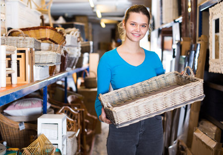 Smiling young woman consumer holding wicker basket in decor items storeの写真素材