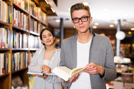 positive young students studying in library, reading and discussing booksの写真素材