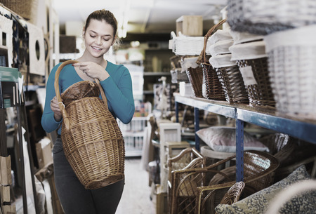 Happy cheerful positive smiling woman consumer holding wicker barrel in decor items store  の写真素材
