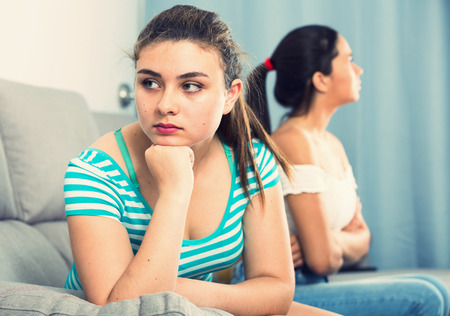Two quarreled girls teenagers ignoring each other on sofa at homeの写真素材