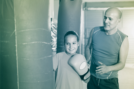 Smiling teenage girl training at gym on punching bag with instructorの写真素材