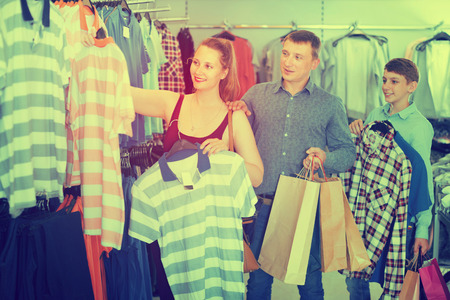 Young family and teen stands near clothes and choosing man shirt in shopの写真素材