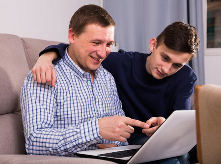 Adult male with his son are resting together and playing on laptop at the home.の写真素材