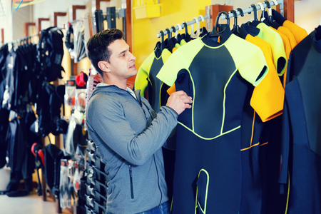 Glad cheerful positive smiling man is standing with modern diving costumes in the store.の写真素材