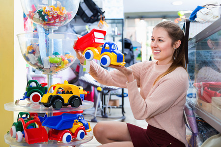Happy glad positive smiling woman buyer choosing toys for baby in the shop of toys for children の写真素材