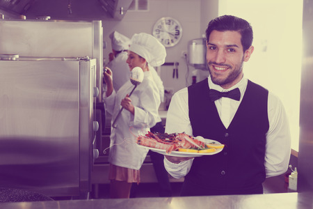 Portrait of handsome waiter with dish of seafood in kitchen on fish restaurant の写真素材