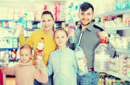 Cheerful family with two daughters holding bottled mineral water in food store の写真素材
