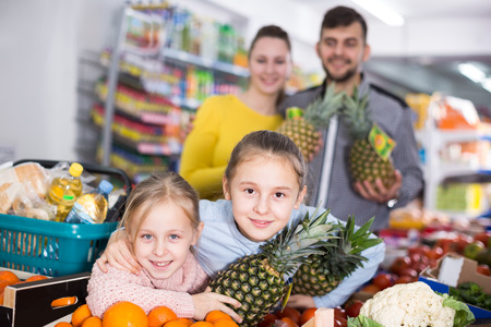Adult parents with two little girls with pineapples in supermarketの写真素材
