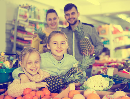 Happy parents with two little girls with pineapples in supermarketの写真素材