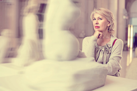 Adult glad  female looking at artwork sculpture in the museum indoorsの写真素材