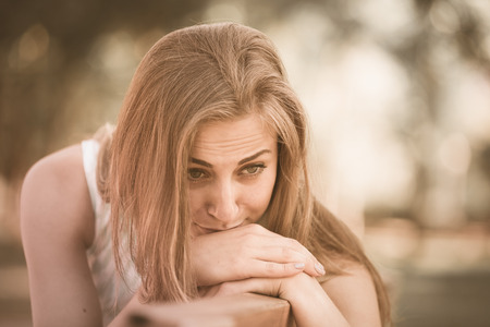portrait of unhappy american young female sitting on bench in gardenの写真素材