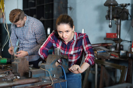Glad cheerful  girl worker is standing near vise equipment in workshop.の写真素材