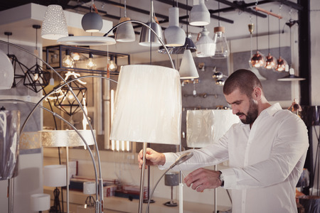 Positive man customer choosing floor lamp in furniture showroomの写真素材