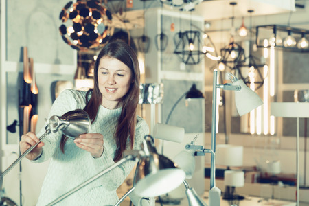Portrait of young female  touching  desk lamp in furniture showroomの写真素材