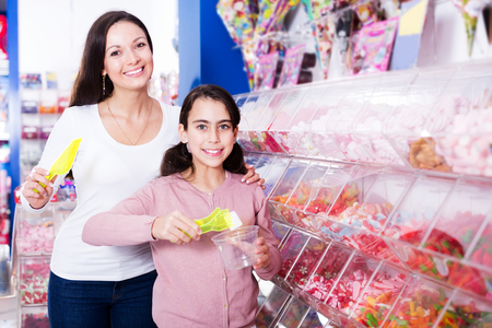 Mother with small daughter choosing fruit jelly for children in store. Focus on womanの写真素材