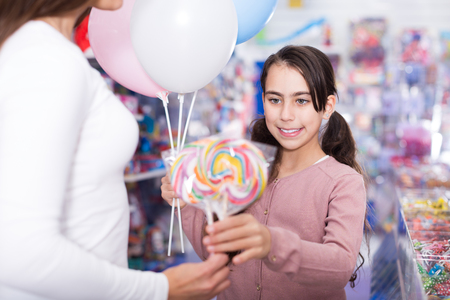 Girl daughter with balloons holding lollipop in candy storeの写真素材