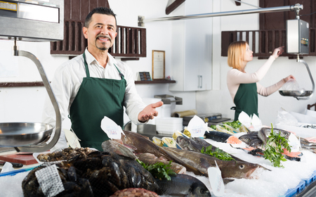 Portrait of two cheerful smiling sellers in aprons in fish section of supermarketの写真素材