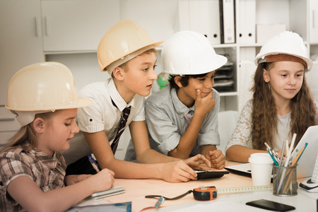Teens in color helmet engineers discussing draft at the tableの写真素材