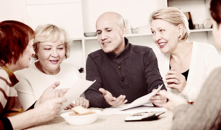Mature women and their friend are reading documents and talking at home.の写真素材