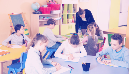 Smiling boys and girls studying and teacher helping at classの写真素材