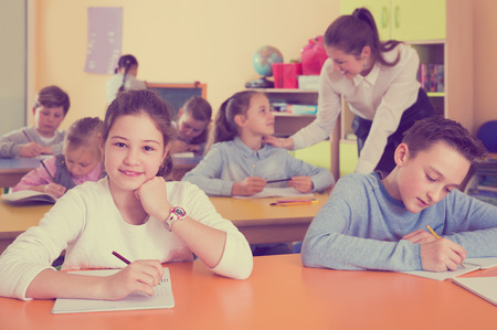 Positive boys and girls studying and woman teacher helping at classの写真素材