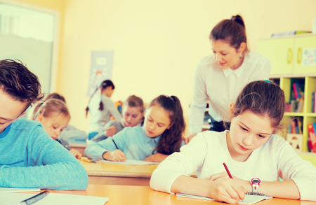 Group of school kids with pens and notebooks studying in classroom with teacherの写真素材