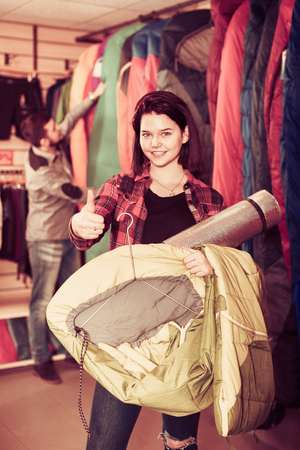 Smiling young couple examining touristic equipment items in sports equipment storeの写真素材