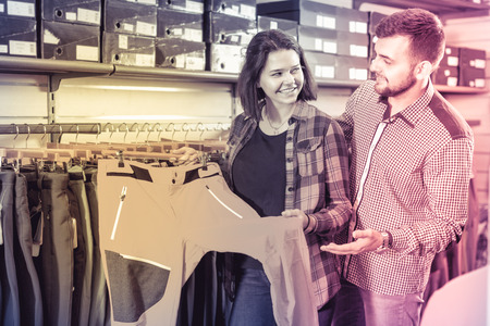 Young smiling  positive couple choosing touristic trousers in sports clothes storeの写真素材